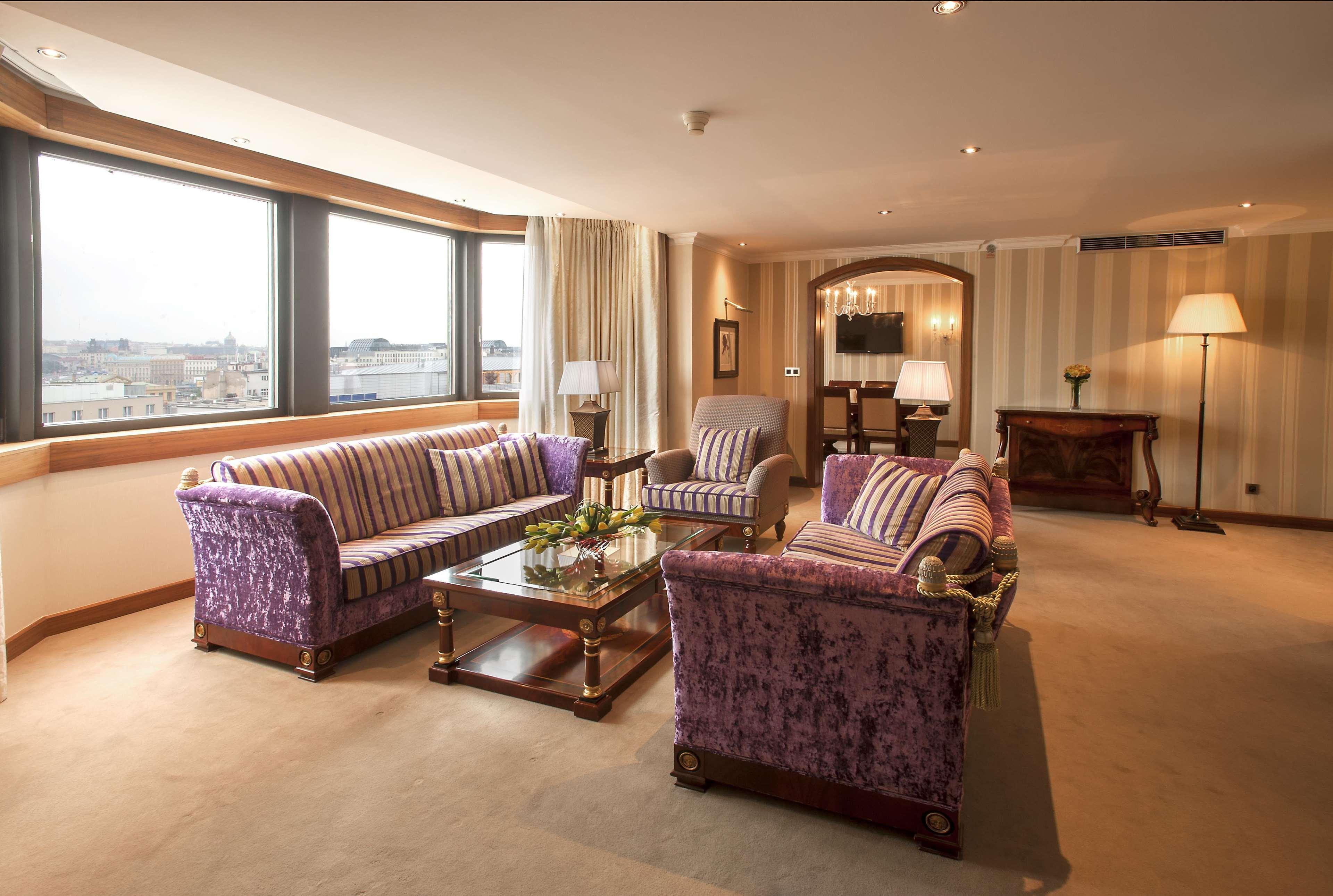 Hilton Prague Hotel Exterior foto The photo shows a spacious, elegantly decorated living room. It features two purple upholstered sofas, one with striped patterns and the other with a solid color, positioned around a glass coffee table. There is a comfortable armchair that complement