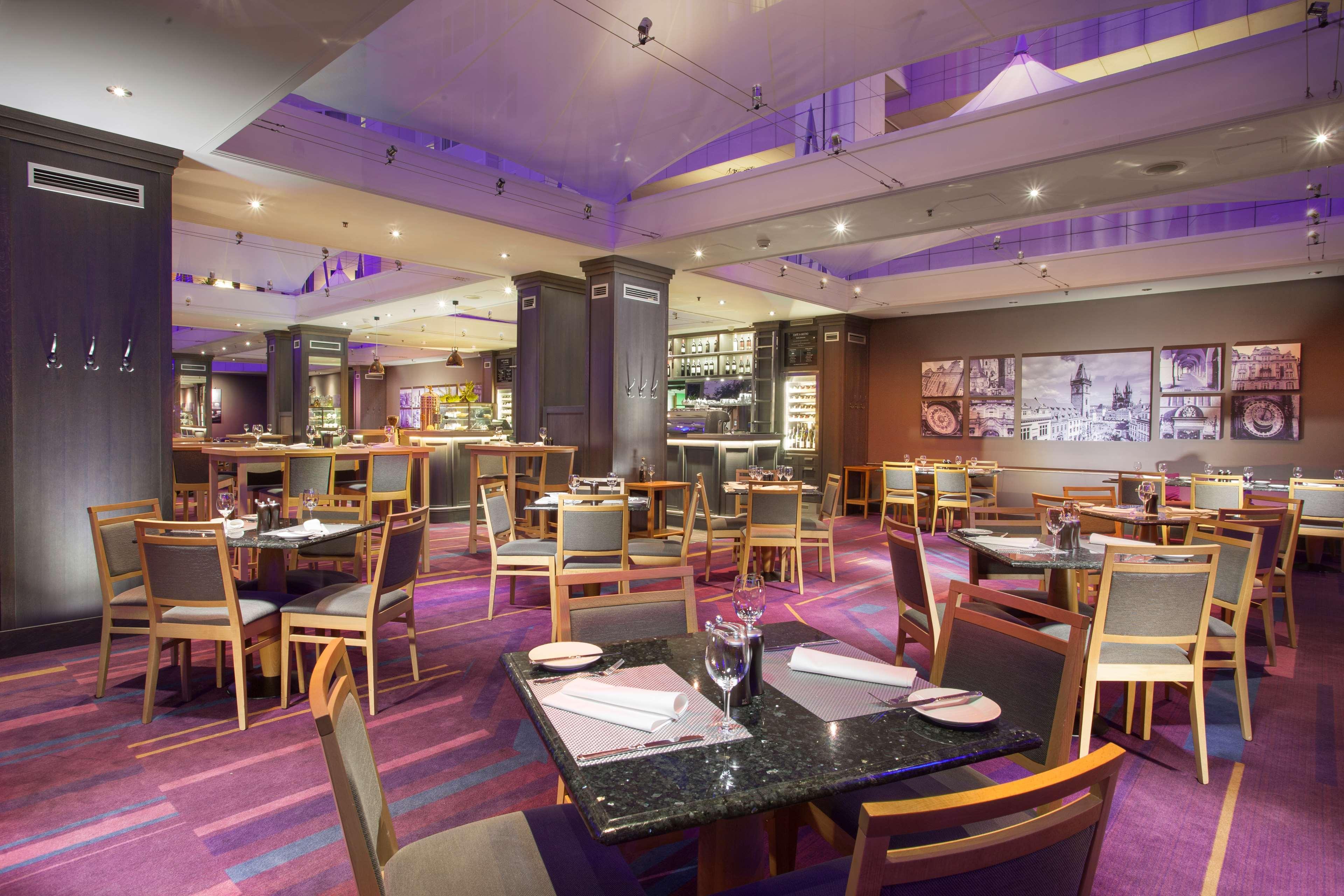 Hilton Prague Hotel Exterior foto The image shows a modern restaurant interiors. It features a spacious dining area with wooden tables and chairs. The tables are set with wine glasses and menus. The flooring has a purple and gray striped design, contributing to a stylish atmosphere. 