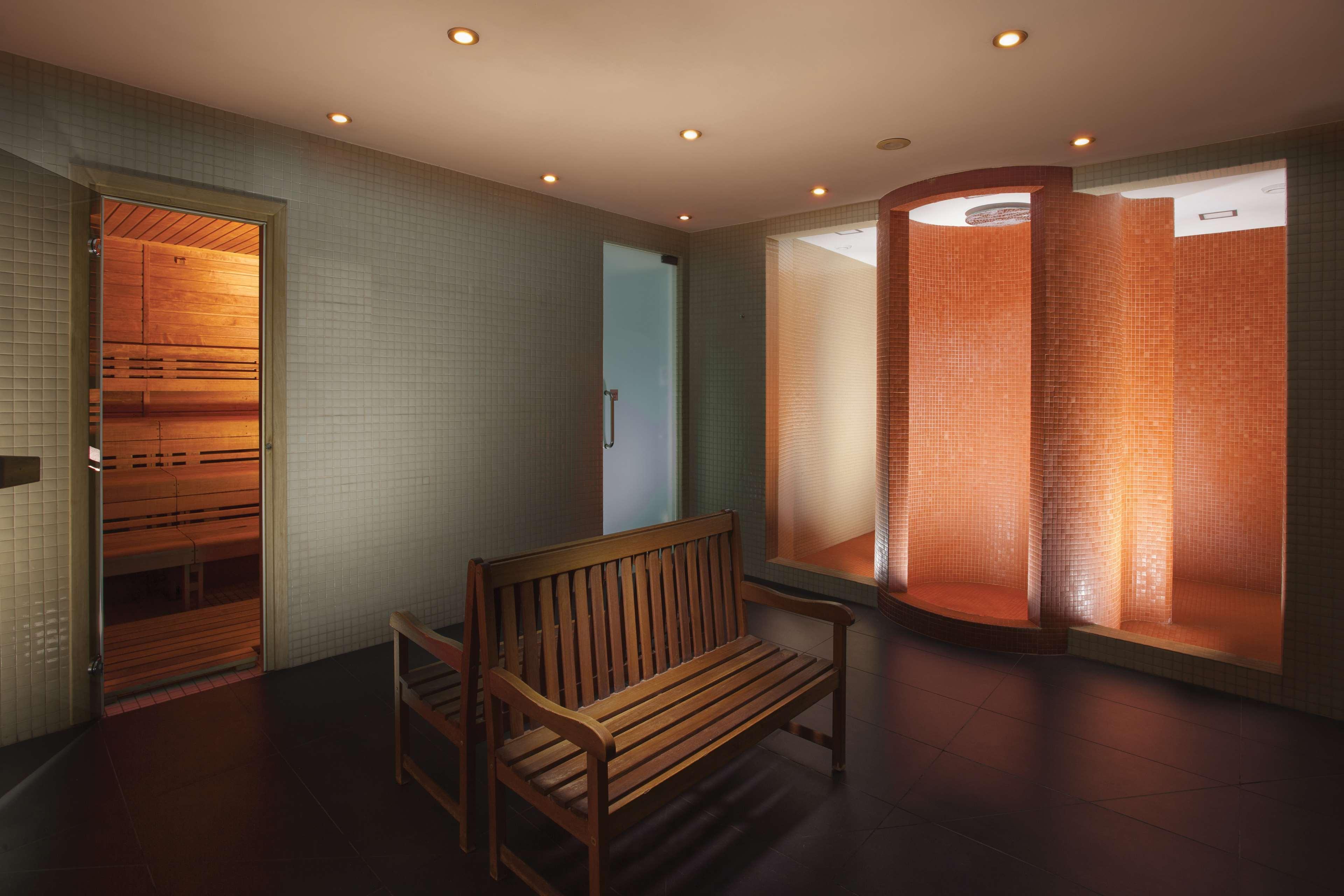 Hilton Prague Hotel Exterior foto The photo depicts a modern spa or wellness area. It features a wooden bench placed in the center, providing seating for relaxation. On the left, there is a door leading into a sauna, characterized by wooden slats. On the right, there are partitions w