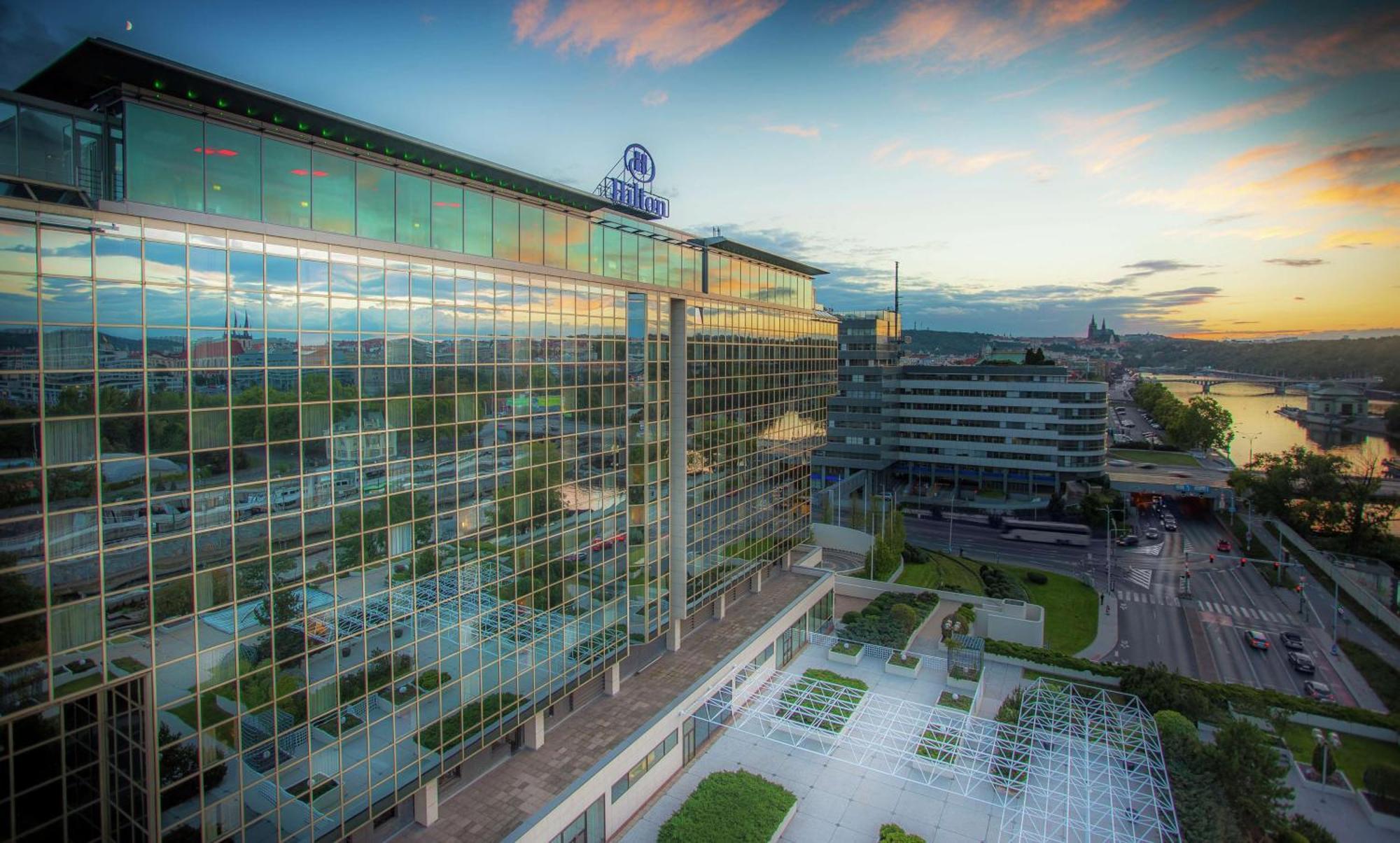 Hilton Prague Hotel Exterior foto The photo depicts a modern, glass-fronted building, likely a hotel or commercial establishment, with a well-maintained exterior and landscaping. The structure features a large amount of reflective glass, allowing it to mirror the surrounding environm